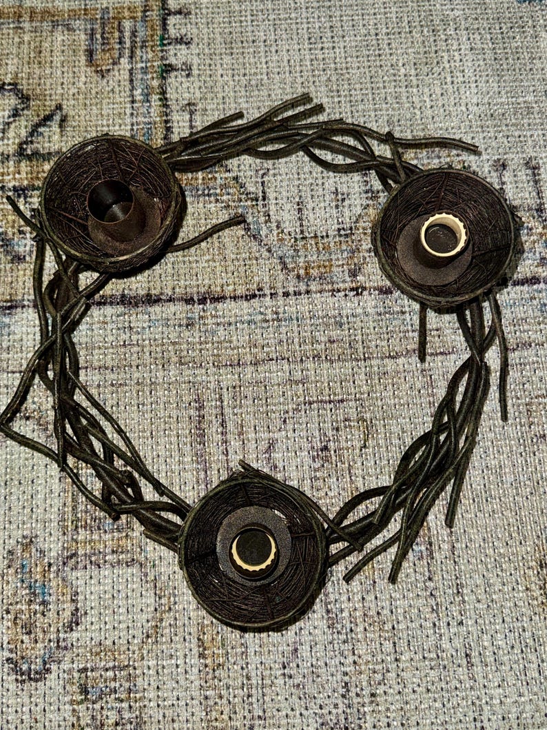 May include: A brown twig wreath with three candle holders. Each holder is a woven basket with a circular opening for a candle.