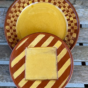Peut inclure: Deux assiettes en céramique, l'une avec un motif à carreaux brun et jaune et l'autre avec des rayures brunes et un carré jaune au centre.