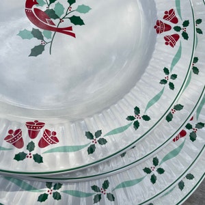 Puede incluir: Un juego de cuatro platos de cena de cerámica blanca con un diseño de acebo y pájaro verde y rojo. Los platos tienen un borde festoneado y un borde elevado.