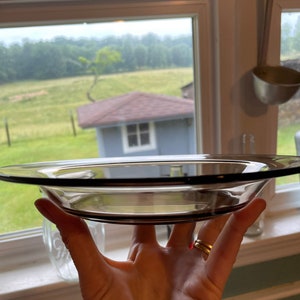 May include: A clear glass bowl with a dark brown rim, held in a hand with a gold ring. The bowl is empty and appears to be made of thick glass.