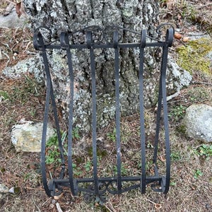 May include: Black wrought iron wall basket with vertical bars and decorative scrollwork. The basket has a curved top and bottom, and is designed to be mounted on a wall or tree. A rustic, vintage-style piece.