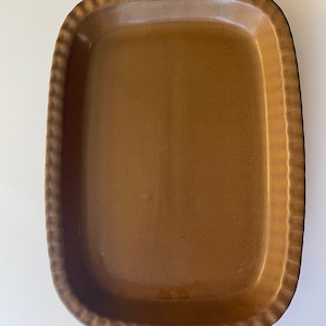 May include: A brown ceramic baking dish with two handles. The dish has a scalloped edge and a smooth, glazed surface.