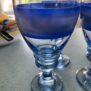 K&ouml;nnte beinhalten: Zwei blaue Weingl&auml;ser aus Glas mit einem matten blauen Band um die Mitte. Die Gl&auml;ser haben einen klaren Boden und einen Stiel.