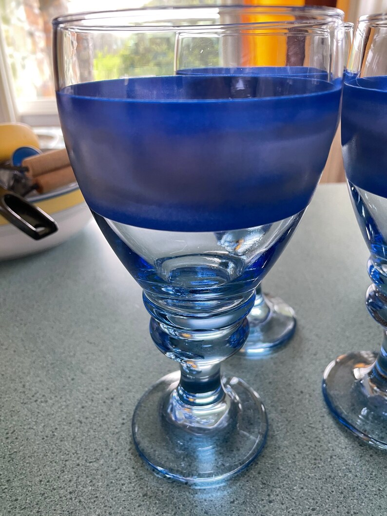 K&ouml;nnte beinhalten: Zwei blaue Weingl&auml;ser aus Glas mit einem matten blauen Band um die Mitte. Die Gl&auml;ser haben einen klaren Boden und einen Stiel.