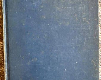 May include: A vintage hardcover book titled "VANITY FAIR" in gold lettering. The book has a blue cover with a textured appearance and signs of age. The book's spine is visible, and the edges show wear.