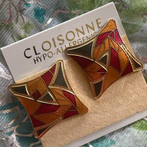 May include: A pair of gold-toned earrings with a geometric design. The earrings are made of cloisonn&eacute;, a technique that uses thin wires to create compartments that are then filled with enamel. The earrings are red, orange, and green.