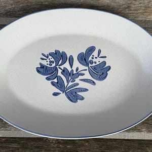 May include: Oval serving platter with a cream-colored base and a blue floral design in the center. The platter has a blue rim and is made of ceramic. The floral design features stylized flowers and leaves.