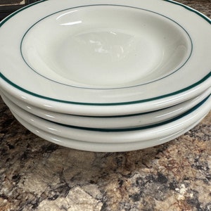 May include: Stack of four white ceramic soup bowls with a green rim.