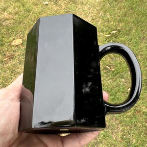 May include: A black hexagonal mug with a handle. The mug is made of ceramic and has a glossy finish.