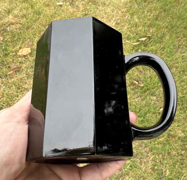 May include: A black hexagonal mug with a handle. The mug is made of ceramic and has a glossy finish.