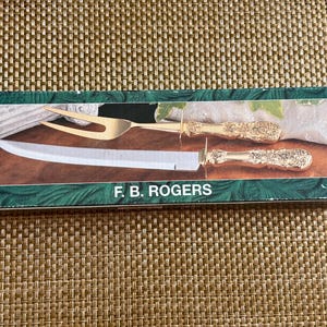 May include: A boxed carving set with a gold-coloured fork and knife, both with decorative handles. The knife has a long, silver blade. The box is green with the text "F. B. ROGERS" in white.