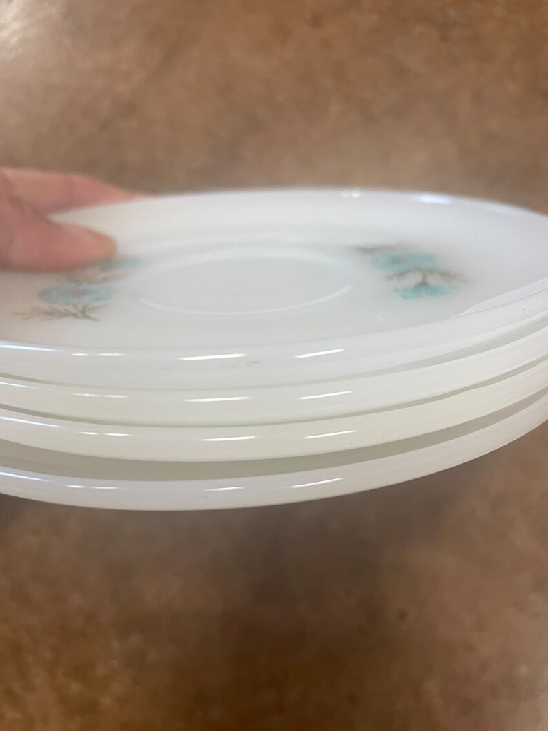 Puede incluir: Una pila de seis platillos de cer&aacute;mica blanca con un delicado dise&ntilde;o floral azul. Los platillos est&aacute;n apilados uno encima del otro, con el platillo superior ligeramente inclinado.