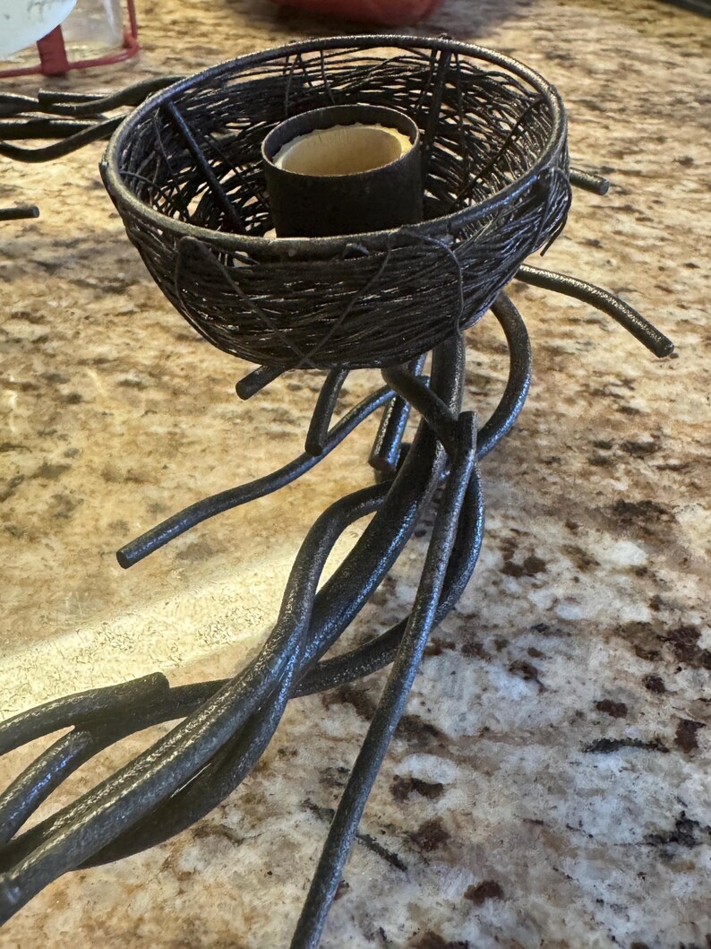 May include: A black metal candle holder with a twig design. The holder has a nest-shaped top with a small candle inside.