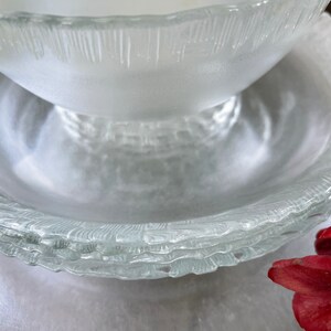 May include: A stack of clear glass bowls and plates with a textured, frosted appearance. The bowls have a rounded shape, and the plates have a wavy, textured rim. The glassware is arranged on a light-colored surface.