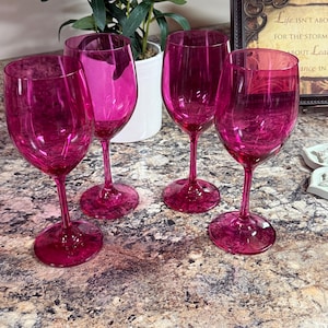 Pode incluir: Um conjunto de quatro taças de vinho magenta translúcidas com bojos arredondados, hastes finas e bases circulares. Cada taça apresenta um acabamento liso e polido com um tom rosa profundo consistente, projetado para servir bebidas em diversas ocasiões.