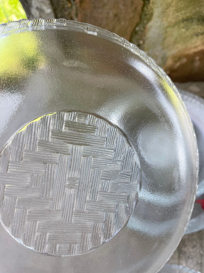 May include: A clear glass plate with a textured surface. The plate has a woven basket pattern on the bottom and a ridged edge. The plate is round and appears to be vintage.