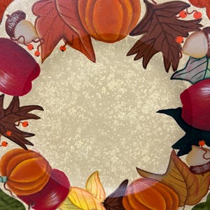 May include: A decorative plate with an autumn theme. The plate is cream coloured with a brown, orange, red, and yellow painted design of pumpkins, leaves, and acorns.