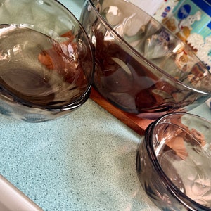 Puede incluir: Cuatro cuencos de vidrio marrón de diferentes tamaños. Los cuencos están apilados uno encima del otro y están sobre una superficie de madera.