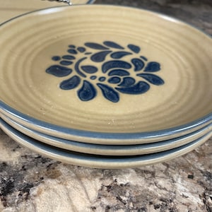 May include: Three stacked blue and white floral patterned ceramic dessert plates with a light brown rim.