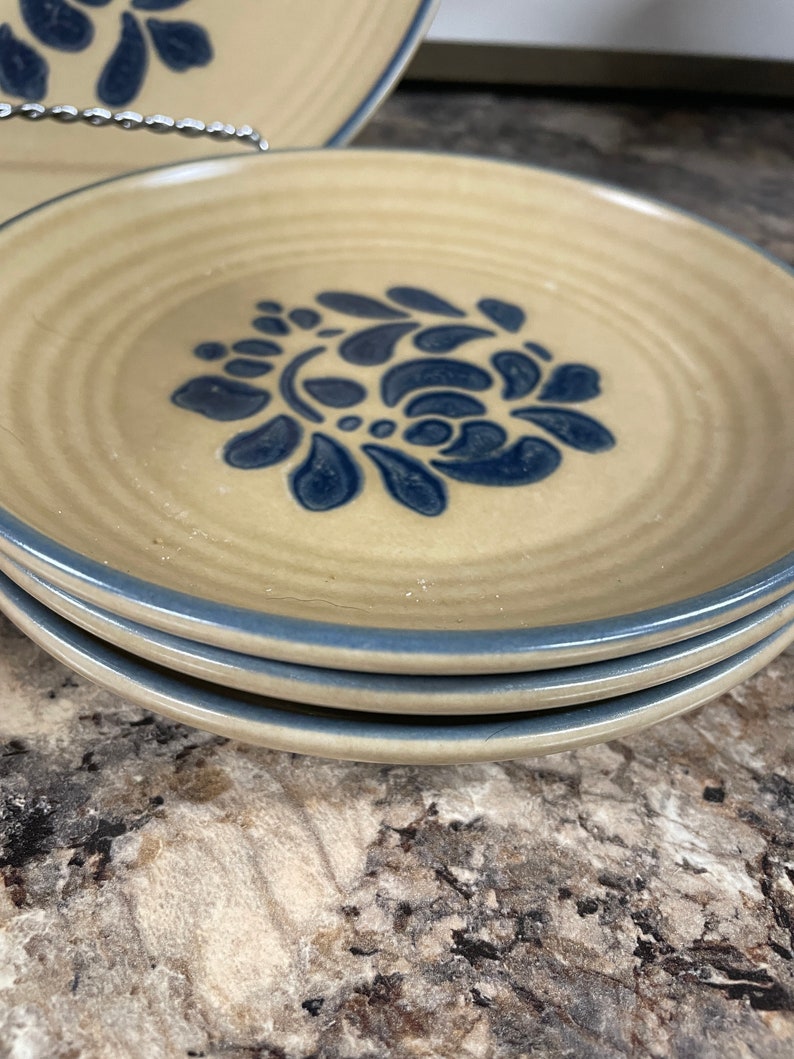 May include: Three stacked blue and white floral patterned ceramic dessert plates with a light brown rim.