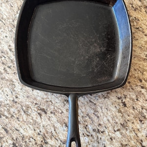 May include: A black cast iron square skillet with a long handle. The skillet is seasoned and ready to use.