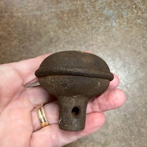May include: A vintage brown metal door knob with a rounded top and a cylindrical base. The knob features a small hole near the base. The metal has a textured, aged appearance, suggesting it is an antique item.