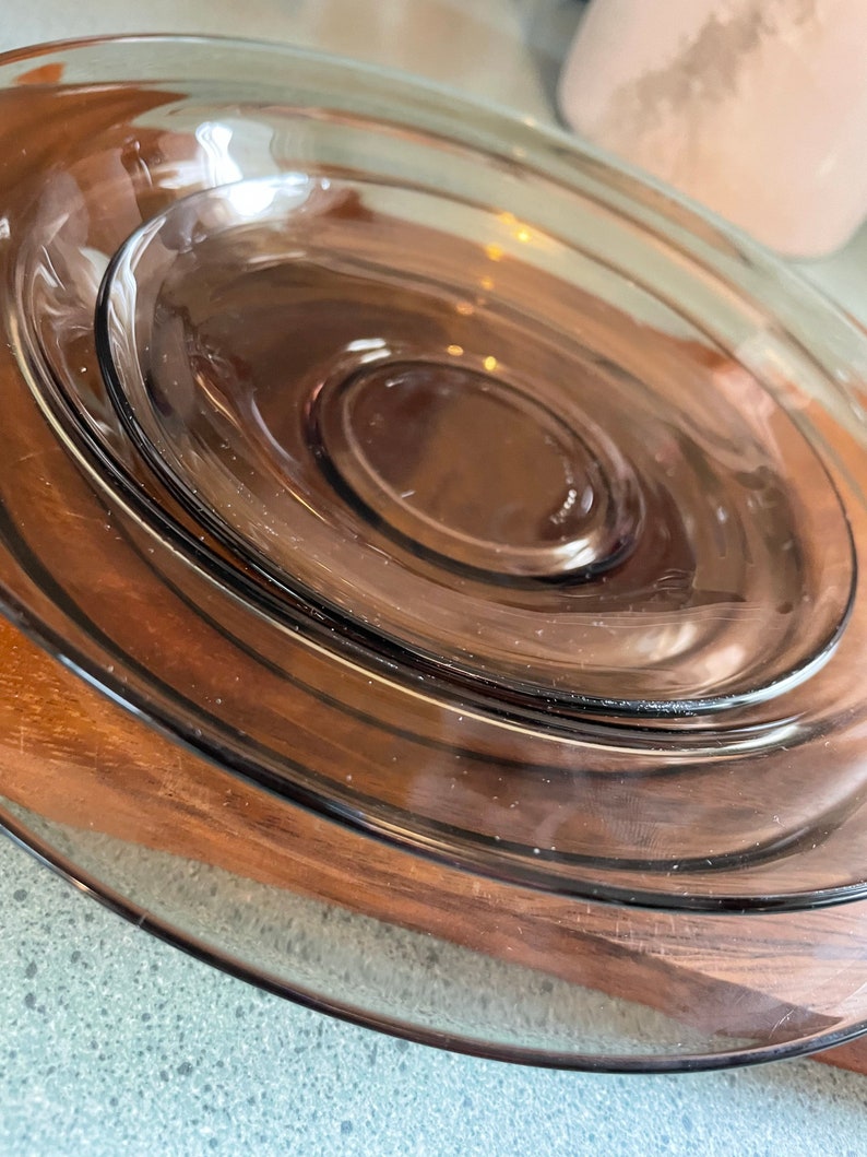 May include: A set of three brown glass plates stacked on top of each other. The plates are round and have a smooth, glossy finish.