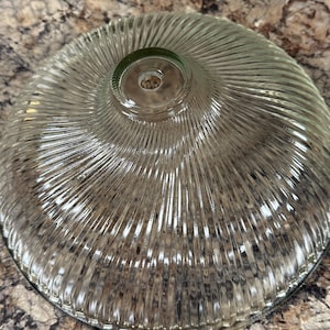 May include: A clear glass lampshade with a ribbed, radial design. The shade has a rounded, bowl-like shape with a small opening at the top. The glass is transparent, allowing light to pass through.
