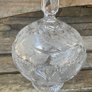 Könnte beinhalten: Eine klare Glasschüssel für Süßigkeiten mit einem mattierten Blumendesign und einem gewölbten Deckel. Die Schüssel hat einen Sockel.