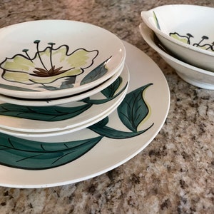 May include: Set of four white ceramic plates with a green and yellow floral design. The plates are stacked on top of each other.