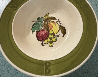May include: A green and white ceramic bowl with a fruit design. The bowl has a green rim and a white interior with a painted design of a bunch of grapes, a peach, and an apple.