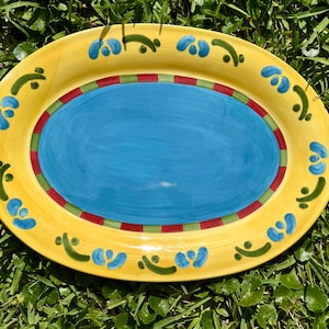 Puede incluir: Una fuente ovalada amarilla con un centro azul y un borde rojo, verde y amarillo. La fuente está decorada con diseños florales verdes y azules.