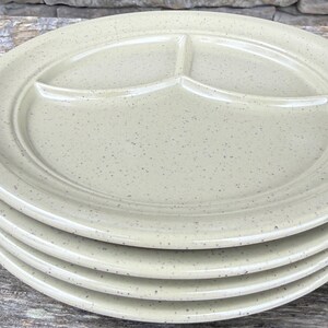 May include: A stack of four round, light beige ceramic plates with a speckled finish. Each plate features a raised rim and is divided into three distinct sections by internal dividers, creating a functional design for serving multiple food items.