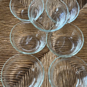 May include: Set of six clear glass bowls, stacked and arranged on a woven surface.
