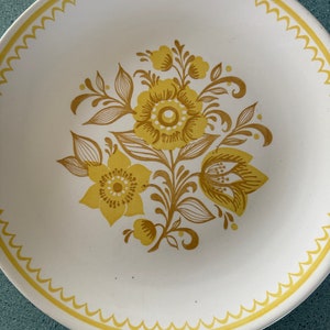 May include: A white ceramic bowl with a yellow floral design. The bowl has a scalloped edge and a yellow rim.