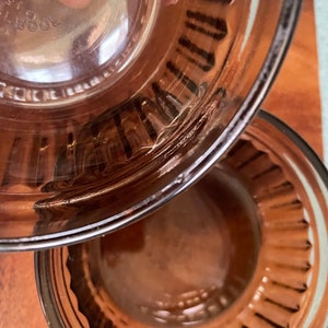 May include: Two brown glass bowls with a fluted rim. The top bowl is upside down, revealing the bottom of the bowl. The bottom bowl is right side up.