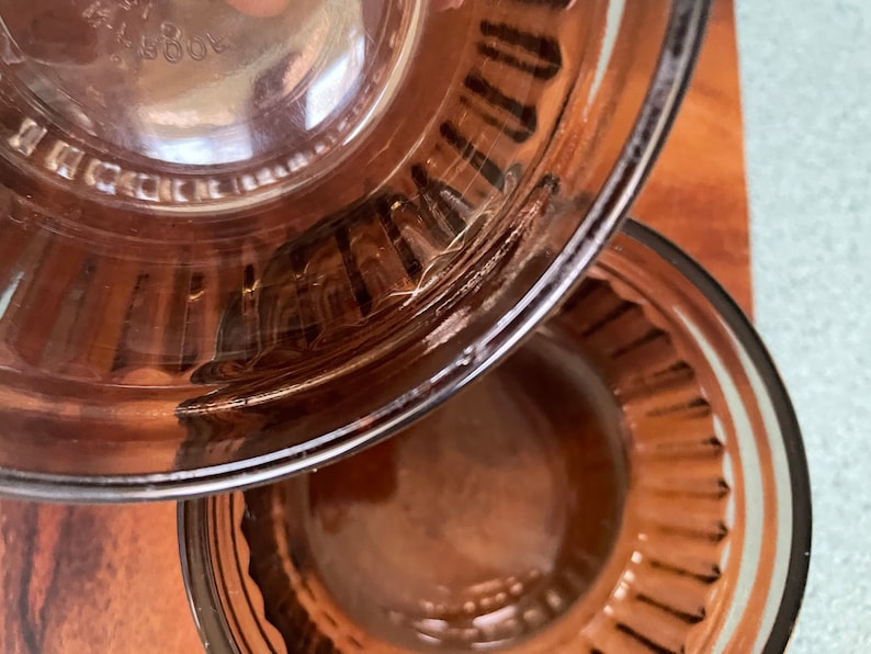 May include: Two brown glass bowls with a fluted rim. The top bowl is upside down, revealing the bottom of the bowl. The bottom bowl is right side up.