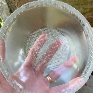 May include: Clear glass bowl with a textured, woven pattern in the center and a scalloped edge. The bowl is transparent, allowing light to pass through. The bowl is likely used for serving food or as a decorative piece.