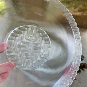 May include: Clear glass serving dish with a woven basket pattern on the base and rim. The dish has a scalloped edge and a circular center. The glass is transparent, allowing light to pass through.