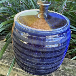 Könnte beinhalten: Eine blaue und braune Keramikdose mit Deckel. Die Dose hat eine strukturierte, gerippte Oberfläche und eine glänzende Oberfläche.