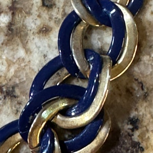 May include: A close-up of a gold and blue chain link bracelet. The links are interlocked and have a shiny finish.