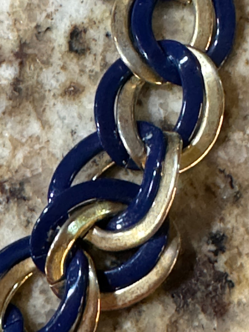 May include: A close-up of a gold and blue chain link bracelet. The links are interlocked and have a shiny finish.