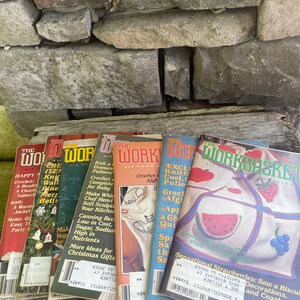 May include: A stack of eight vintage craft magazines with colorful covers featuring knitting, crocheting, and other crafts. The magazines are titled "The Workbasket" and "The Work and Home".