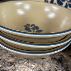 May include: Three stacked beige ceramic bowls with a blue floral design and a blue rim.