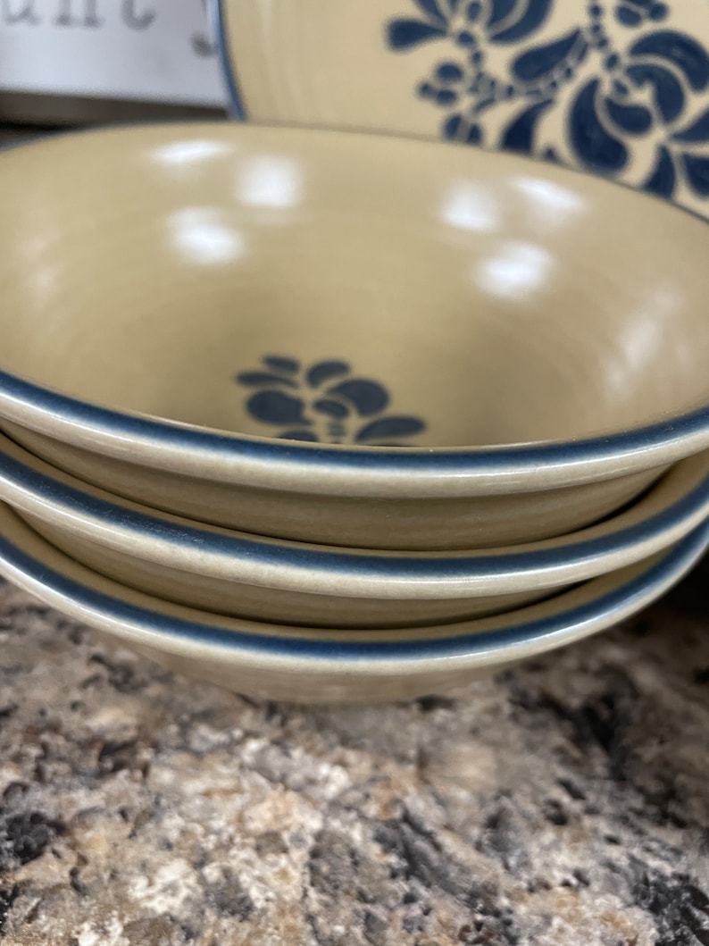 May include: Three stacked beige ceramic bowls with a blue floral design and a blue rim.
