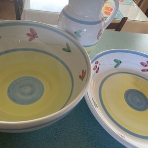May include: A set of three ceramic kitchenware items in a yellow, blue, and green floral pattern. The set includes a large bowl, a smaller bowl, and a pitcher.