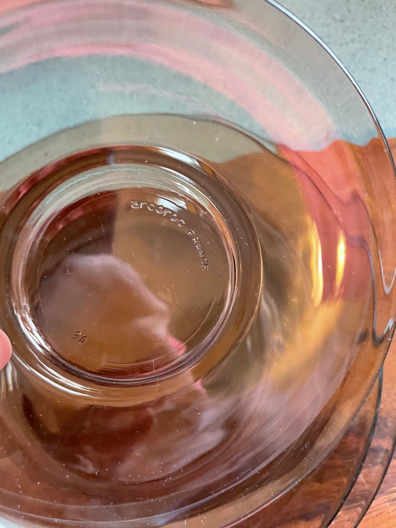 May include: A clear glass plate with a brown tint. The plate has a raised edge and a smooth surface. The bottom of the plate has the text "arc international" printed on it.