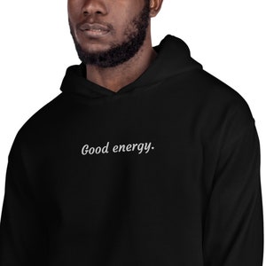 May include: Black hoodie with the phrase "Good energy" in white script across the chest. The hoodie has a drawstring hood and a kangaroo pocket. The fabric appears soft and comfortable, suitable for casual wear.