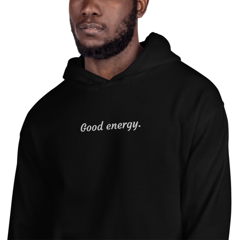 May include: Black hoodie with the phrase "Good energy" in white script across the chest. The hoodie has a drawstring hood and a kangaroo pocket. The fabric appears soft and comfortable, suitable for casual wear.