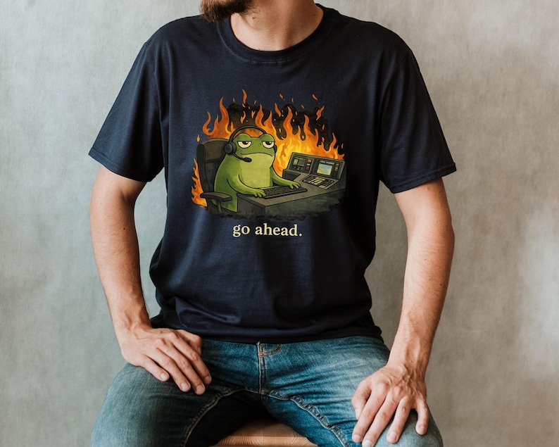 funny 911 dispatcher shirt for men and women, office frog with on a call sitting at his desk surrounded by fire, the words "go ahead." are written below the scene